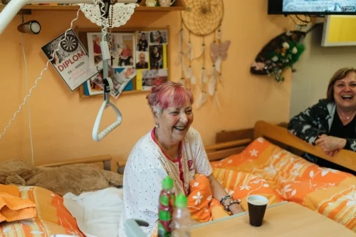 Giving Patients a Voice Woman laughing in a bedroom with another woman while discussing health insurance tips.