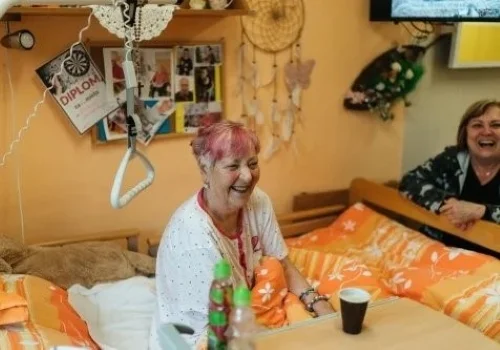 Woman laughing in a bedroom with another woman while discussing health insurance tips.